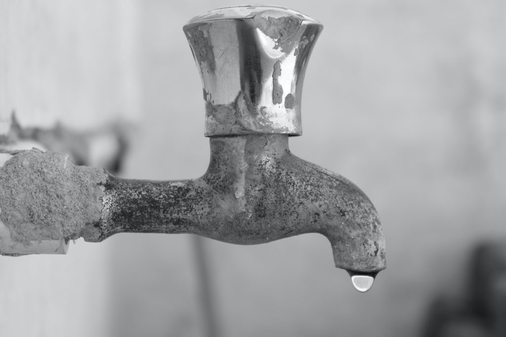 a limescale encrusted tap with a single drop of water hanging from it, emphasising the cosmetic impact of limescale and hard water