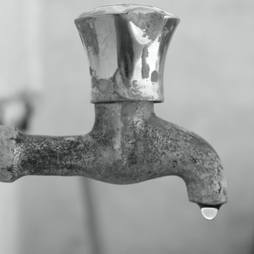 a limescale encrusted tap with a single drop of water hanging from it, emphasising the cosmetic impact of limescale and hard water