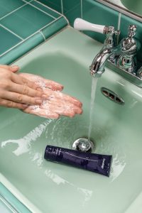 a person washing their hands in a sink with lathered soap tying into the link between soft water and skin
