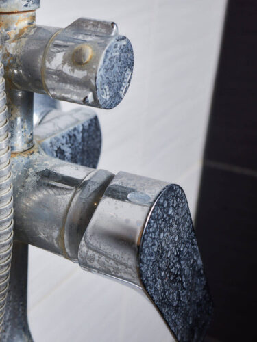 A thin stream of hard water flows from an old tap aerator. Old Bathroom Sink Faucet contaminated with calcium and grime