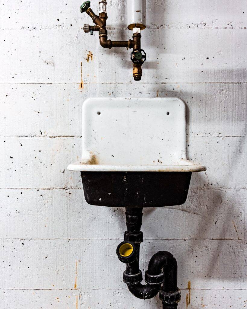 grubby white sink on white wall suggesting that cleaning is important and posing the question are water softeners necessary