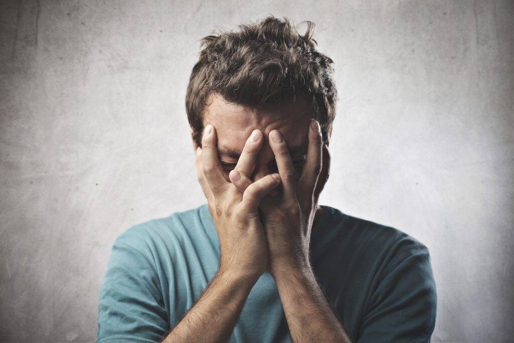 man in blue shirt clutching face in pain from a kidney stone