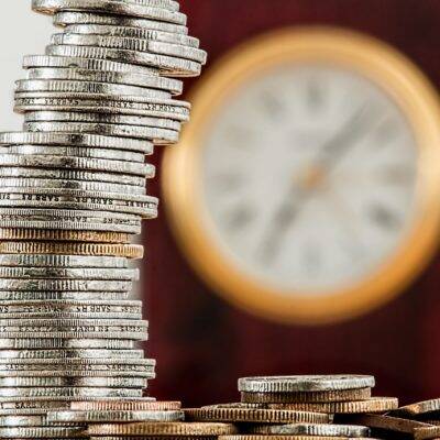 a stack of coins in the foreground with a clock in the background suggesting that a Halcyan water conditioner can save both time and money